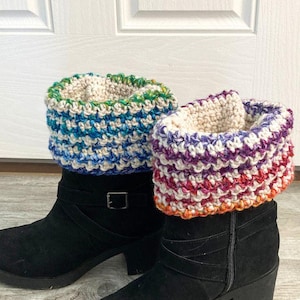 May include: Two pairs of black ankle boots with colorful, crocheted boot cuffs. The cuffs feature a striped pattern in shades of blue, green, purple, red, and orange. The boots have a buckle and a zipper.