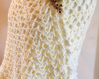Puede incluir: Un chal de ganchillo blanco con un broche decorativo dorado y rojo.