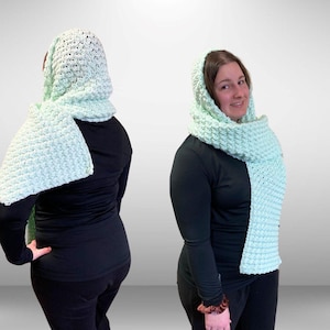 May include: A light green crocheted hooded scarf with a textured stitch pattern. The scarf is worn by a person with brown hair and a black shirt.