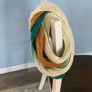 Op de afbeelding: Een gehaakte oneindige sjaal met strepen in crème, mosterdgeel en turquoise.