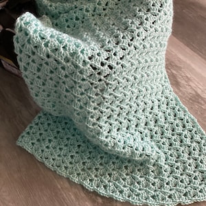 May include: A light blue crocheted baby blanket with a delicate open stitch pattern.
