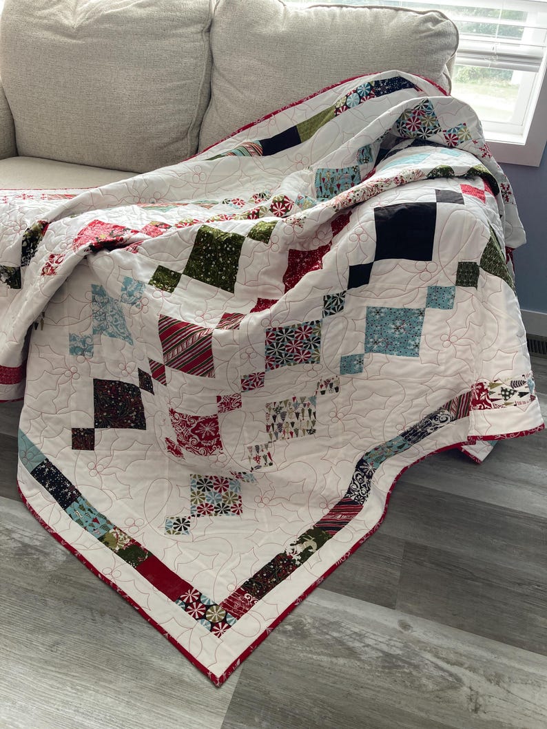 May include: A white quilt with a red, green, and blue patchwork design. The quilt is folded and draped over a white couch.