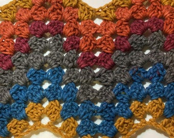 May include: A close-up of a crocheted fabric with a wavy edge. The fabric is made with different coloured yarn, including orange, red, grey, blue, and yellow.