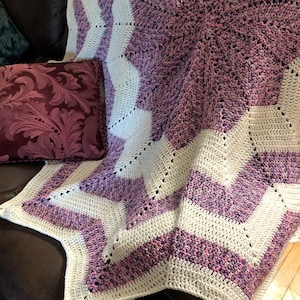 May include: A crocheted blanket with a starburst pattern in shades of purple and white.