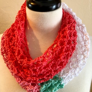 May include: A crocheted infinity scarf in coral, mint green, and white. The scarf is made with a delicate open stitch pattern.