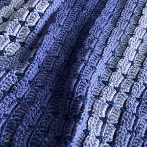 May include: A crocheted blanket with a gradient of blue and purple hues. The blanket has a textured pattern and a crocheted border.