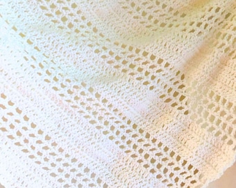 May include: A cream-colored, open-weave crochet shawl. The shawl has a triangular shape with a delicate, lacy pattern. The texture is soft and airy, with a subtle gradient of pink and yellow hues. The website address "Patternprincess.com" is visible.