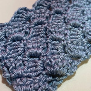 May include: A close-up of a crocheted fabric in a light blue color. The fabric is made of a series of connected loops, creating a textured pattern.