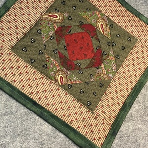 May include: A green, red, and brown patchwork quilt square with a paisley pattern. The square is surrounded by a green border.