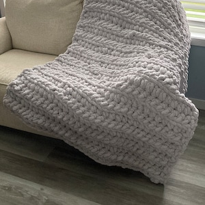 Peut inclure: Une couverture en tricot &eacute;pais et moelleuse de couleur grise, pos&eacute;e sur un canap&eacute;.