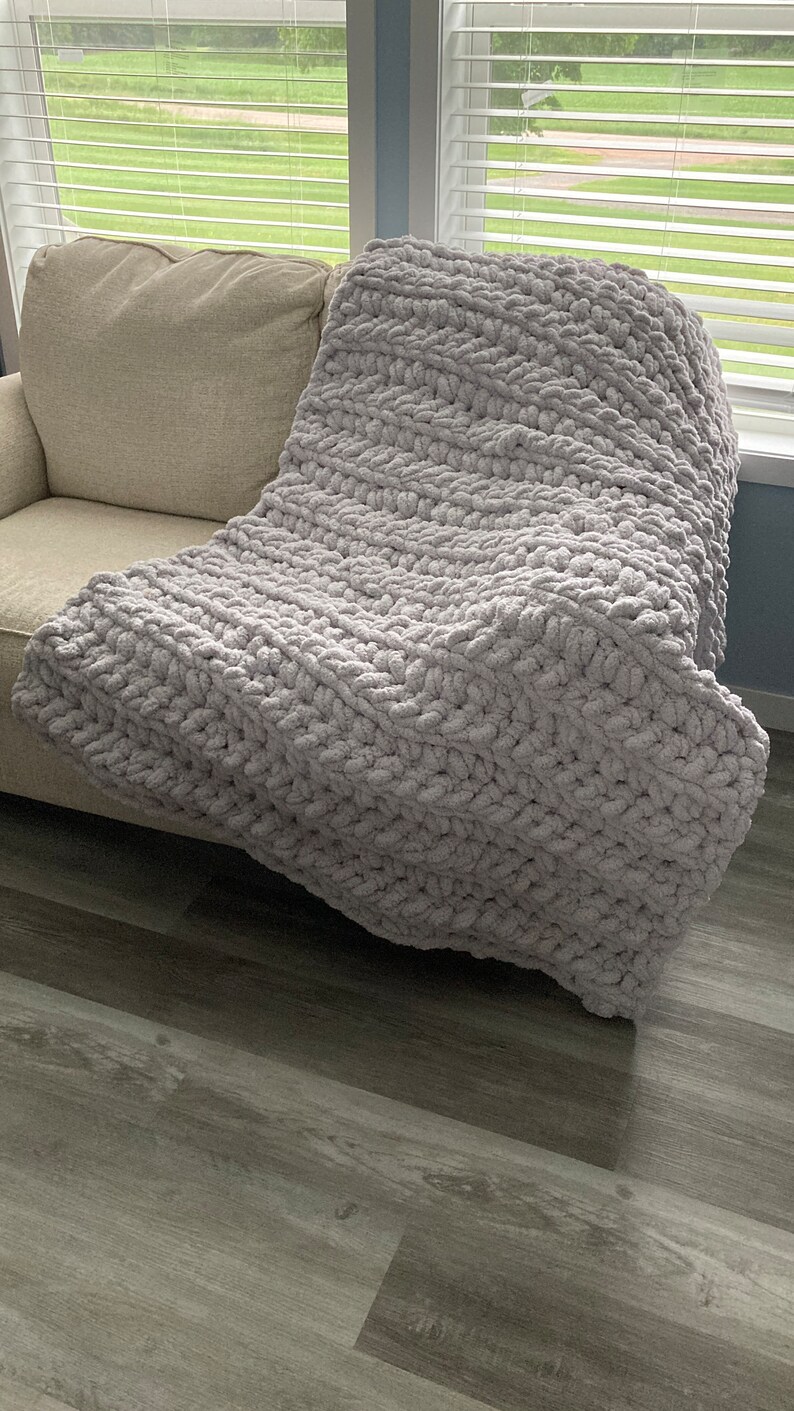 Peut inclure: Une couverture en tricot &eacute;pais et moelleuse de couleur grise, pos&eacute;e sur un canap&eacute;.