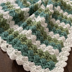 May include: A crocheted baby blanket in white, green, and teal with a scalloped edge.