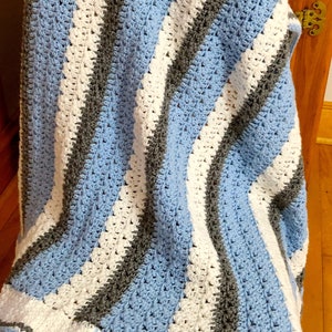 May include: A blue, white, and gray striped crocheted blanket draped over a wooden chair.