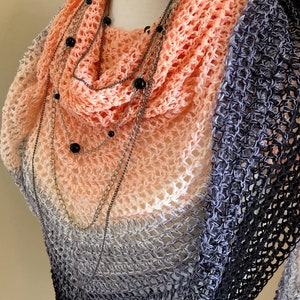 May include: A peach and grey ombre crochet shawl with a black beaded chain necklace.