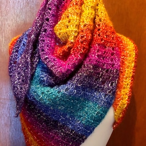 Könnte beinhalten: Ein Regenbogen-Häkel-Schal mit einem zarten Muster. Der Schal ist über eine weiße Schaufensterpuppe gelegt.