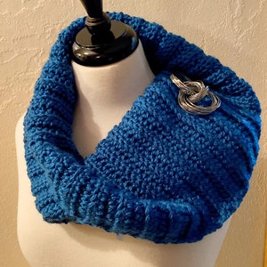 May include: A blue crocheted infinity scarf with a silver metal ring accent.