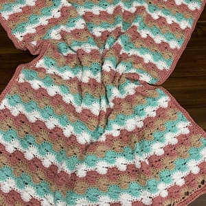 Puede incluir: Una manta de bebé tejida a crochet con un patrón de rayas en tonos rosa, blanco y turquesa.