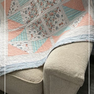 Puede incluir: Una colcha azul claro y rosa con un estampado de zorros. La colcha est&aacute; doblada y drapeada sobre un sof&aacute; beige. El texto "Patternprincess.com" es visible en la esquina inferior derecha de la imagen.