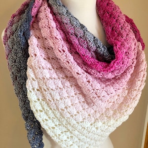 Può includere: Uno scialle all'uncinetto con un gradiente di colori rosa, bianco e grigio. Lo scialle è drappeggiato su un manichino.