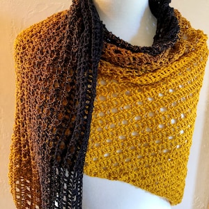 May include: A crocheted shawl with a gradient of brown to yellow. The shawl is draped over a white mannequin.