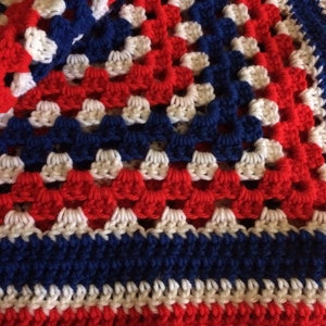 May include: A crocheted blanket with a red, white, and blue pattern. The blanket is made with a granny square stitch.