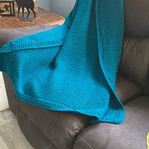May include: A teal blue crocheted throw blanket draped over a brown leather couch.