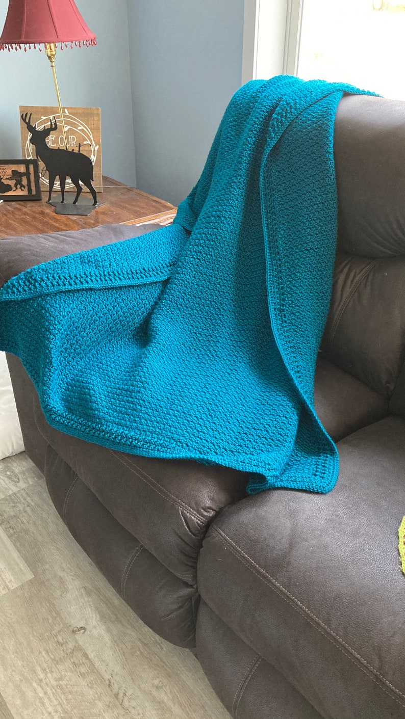 May include: A teal blue crocheted throw blanket draped over a brown leather couch.