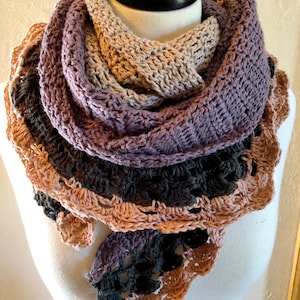 May include: A crocheted scarf in shades of brown, purple, and black. The scarf is made with a textured stitch and has a scalloped edge.