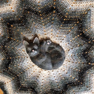 May include: A black and white crocheted blanket with a black cat figurine in the center.