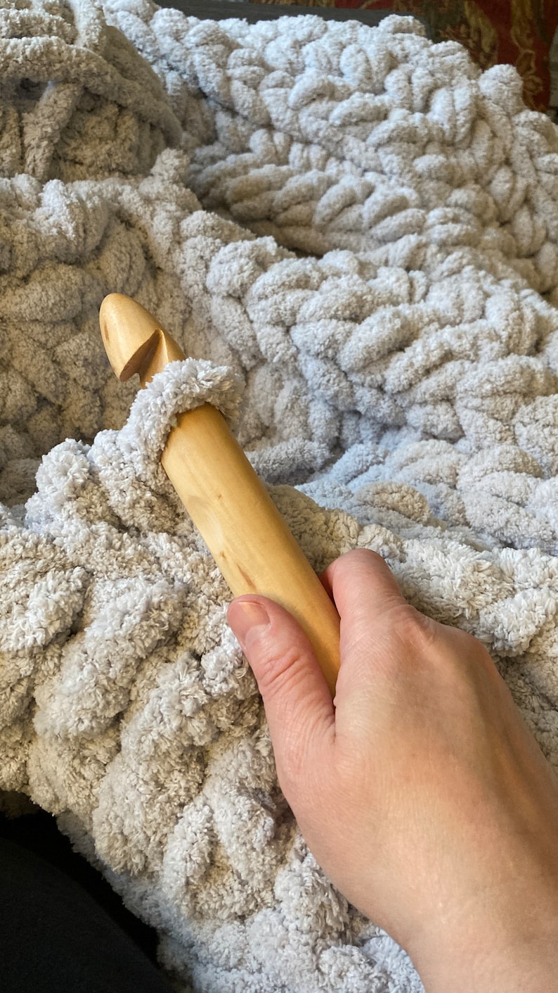 Peut inclure: Gros plan sur un crochet en bois utilis&eacute; pour cr&eacute;er une couverture en tricot &eacute;pais. La couverture est de couleur gris clair et a une texture douce et moelleuse.