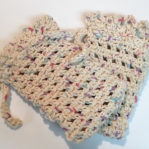 May include: A crocheted scrubbie with a drawstring closure. The scrubbie is made with a beige yarn with pink, blue, and purple flecks.