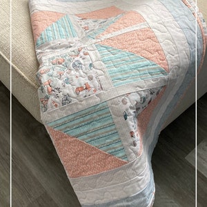 Puede incluir: Una colcha de retazos rosa y azul con un tejido estampado de zorros y b&uacute;hos. La colcha est&aacute; doblada en un sof&aacute; marr&oacute;n claro y un suelo de madera.