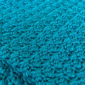 May include: Close-up of a teal blue crocheted fabric with a textured pattern.