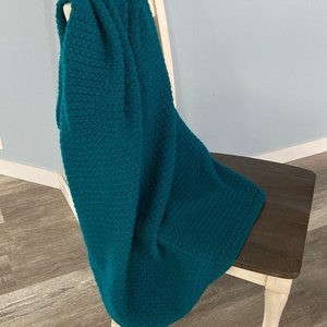 May include: A teal blue crocheted throw blanket draped over a wooden chair with white legs.