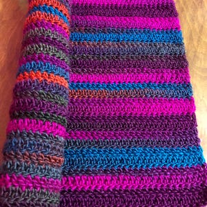 May include: A striped crocheted scarf in shades of purple, blue, brown, and orange. The scarf is rolled up and the ends are visible.