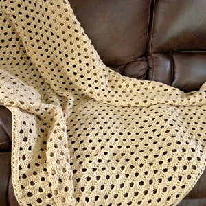 May include: A beige crocheted throw blanket with a diamond pattern, draped over a brown leather sofa.