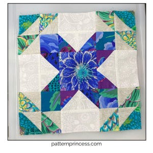 May include: A colorful quilt block featuring a central blue floral design. The block is composed of various fabric patterns, including floral prints, triangles, and solid colors in shades of blue, purple, green, and cream. The website patternprincess.com is visible.