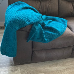 May include: A teal blue crocheted throw blanket draped over a brown leather couch.