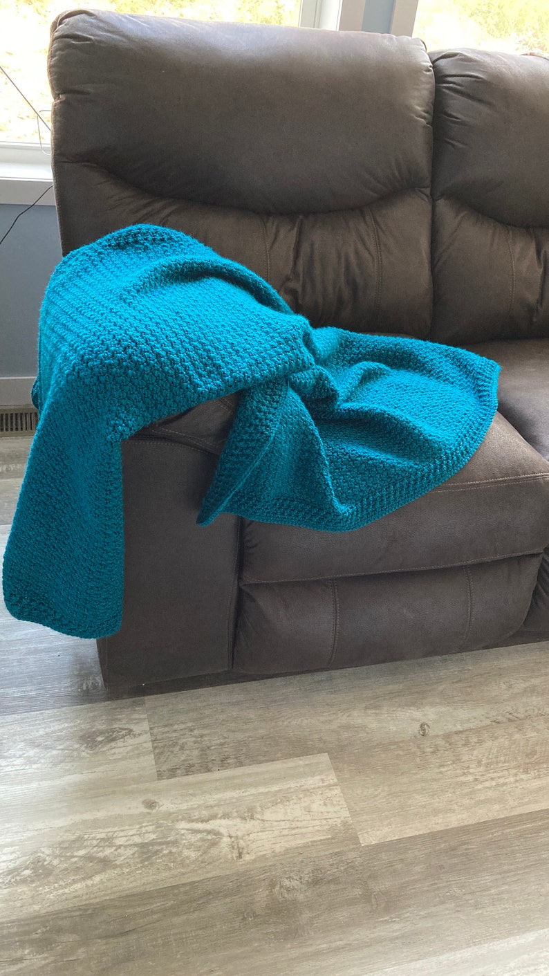 May include: A teal blue crocheted throw blanket draped over a brown leather couch.