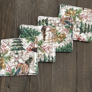 May include: Set of four quilted fabric pot holders featuring a Christmas theme with a white background, green trees, red berries, gold bells, and brown deer.