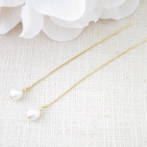 May include: A pair of gold chain earrings with a white pearl at the end of each chain.