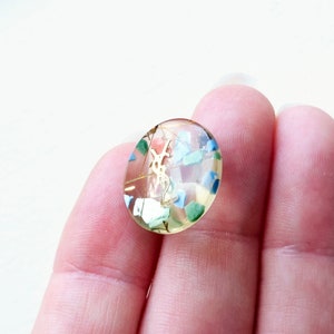 Può includere: Cabochon ovale in resina trasparente con un logo YSL dorato e macchie colorate di blu, verde e bianco.
