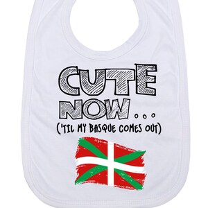 Könnte beinhalten: Weißer Baby-Lätzchen mit schwarzem Text, der "Cute Now... (Til my Basque comes out)" lautet, und einer rot-grün-weißen baskischen Flagge.