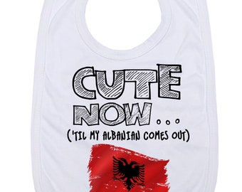 May include: White baby bib with black text that reads "Cute Now... (Til My Albanian Comes Out)" and a red and black Albanian flag.