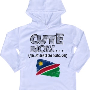 May include: White long-sleeve hooded sweatshirt with the text "CUTE NOW... (TIL MY NAMIBIAN COMES OUT)" and a graphic of the Namibian flag.