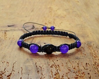 May include: A black braided bracelet with purple and black beads. The bracelet has a simple design and is made with natural materials.