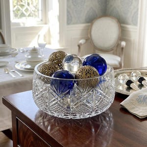 May include: A clear cut-glass bowl with a geometric diamond pattern filled with decorative spheres. The collection includes smooth cobalt blue glass orbs, clear glass spheres, and intricate gold-toned metal filigree balls.