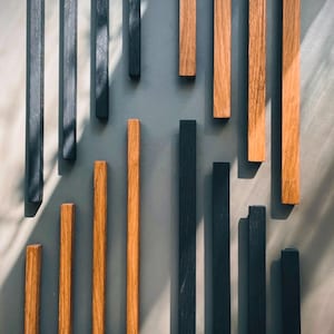 Peut inclure: Une collection de chevilles en bois dans des finitions noires et bois naturel. Les chevilles sont disposées en grille sur un fond gris.