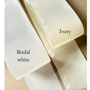 Puede incluir: Dos tiras anchas de cinta de sat&eacute;n lisa y brillante dispuestas una al lado de la otra. Una tira est&aacute; etiquetada como Bridal white y presenta un tono blanco brillante y fr&iacute;o. La otra tira est&aacute; etiquetada como Ivory y muestra un color crema.