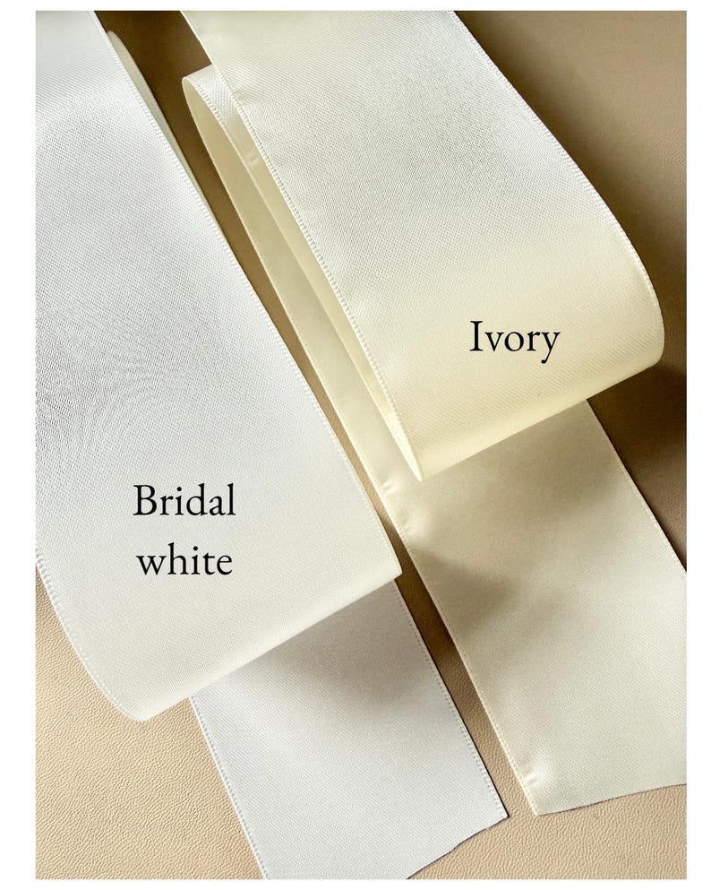 Puede incluir: Dos tiras anchas de cinta de sat&eacute;n lisa y brillante dispuestas una al lado de la otra. Una tira est&aacute; etiquetada como Bridal white y presenta un tono blanco brillante y fr&iacute;o. La otra tira est&aacute; etiquetada como Ivory y muestra un color crema.